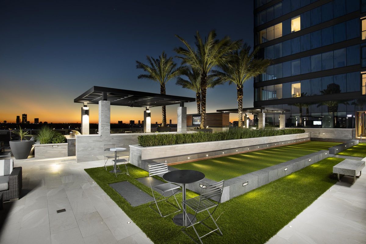 Rooftop lounge with palm trees and seating at sunset, overlooking cityscape.