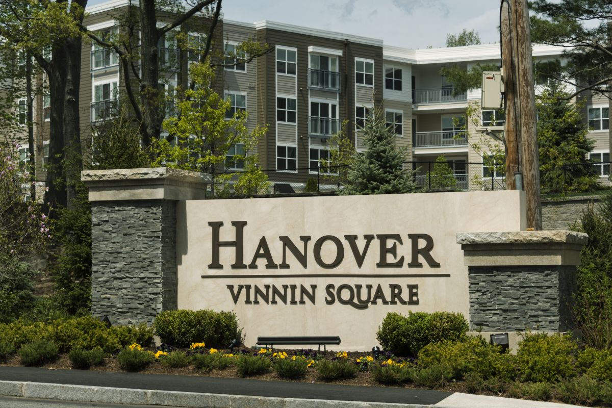 Stone sign reading "Hanover Vinnin Square" in front of modern apartment buildings and landscaped greenery.