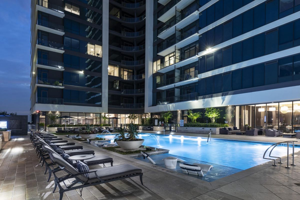 Modern apartment building with a lit swimming pool and lounge chairs at dusk.