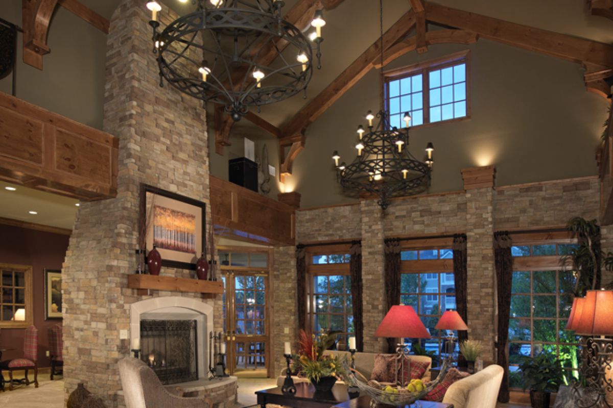 Spacious living room with high wooden beams, stone fireplace, chandeliers, and cozy seating area.