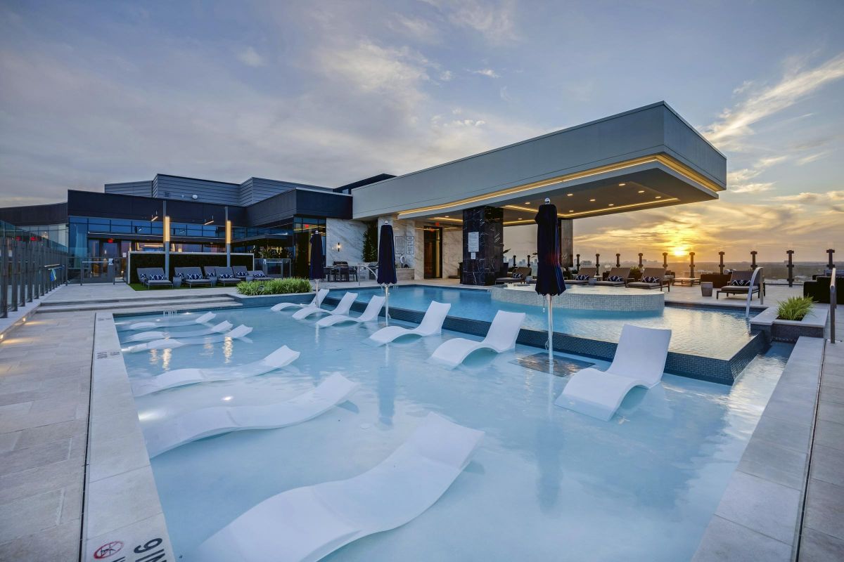 Modern rooftop pool with submerged loungers and umbrellas overlooking a sunset.
