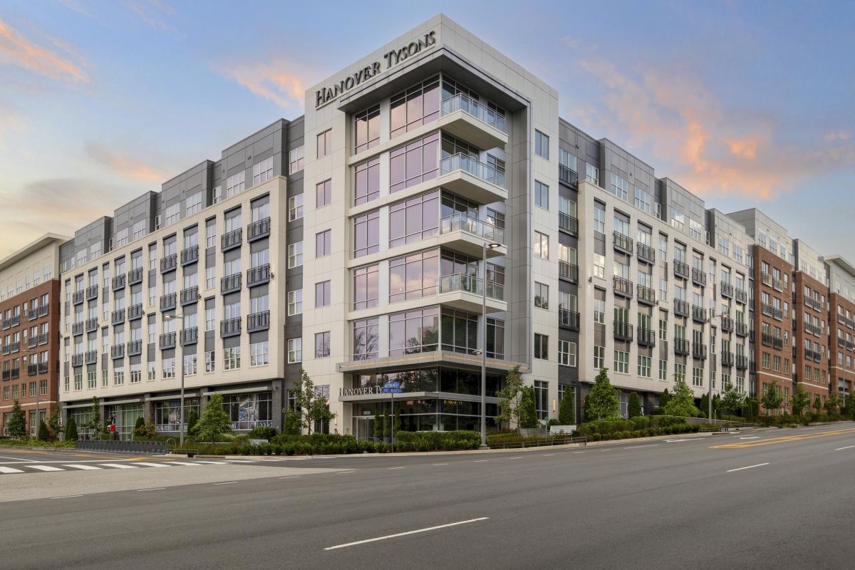 Modern multi-story apartment building with large windows and balconies, adjacent to a wide street at sunset.