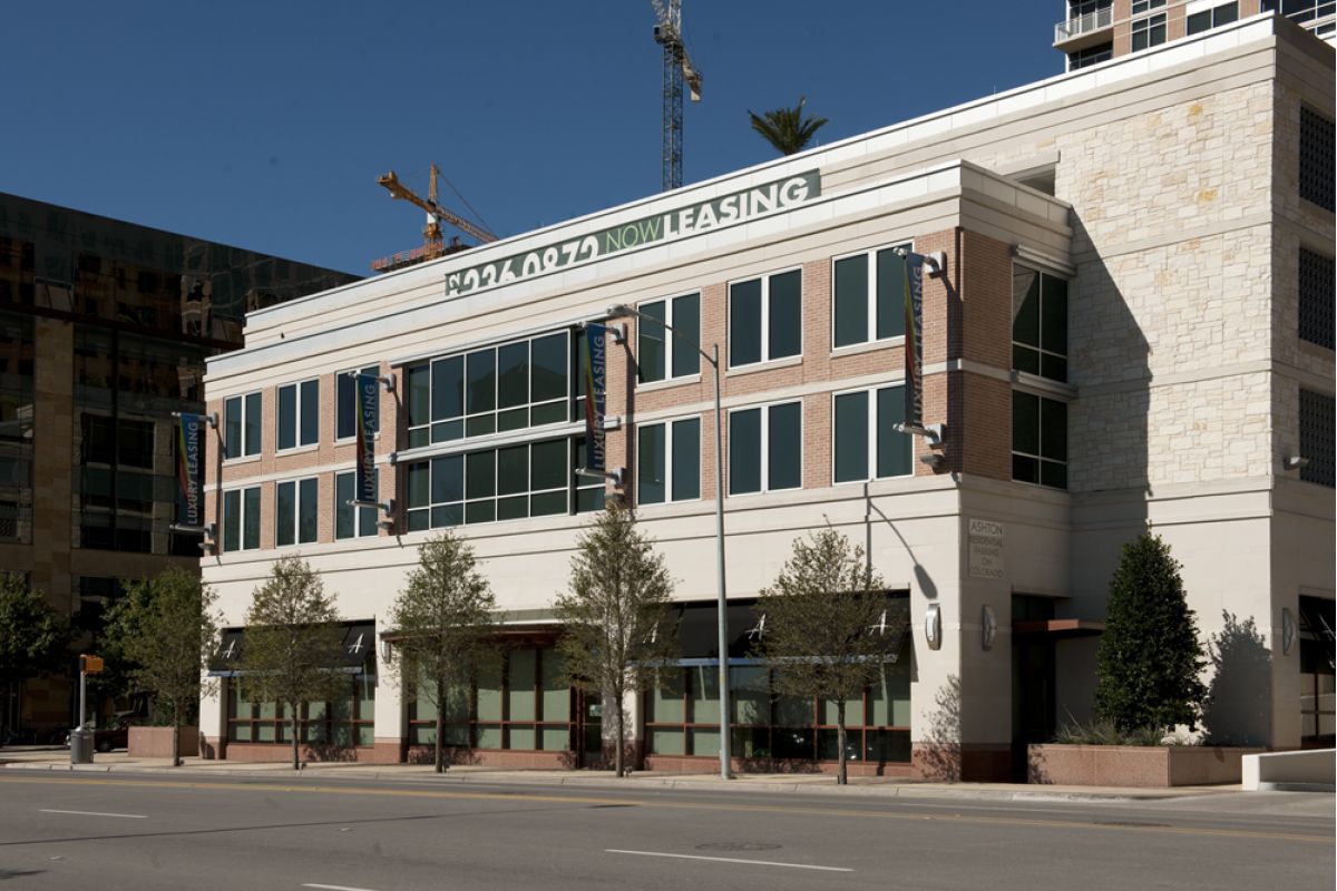 Three-story commercial building with large windows facing the street, featuring a “Now Leasing” sign at Ashton Austin.