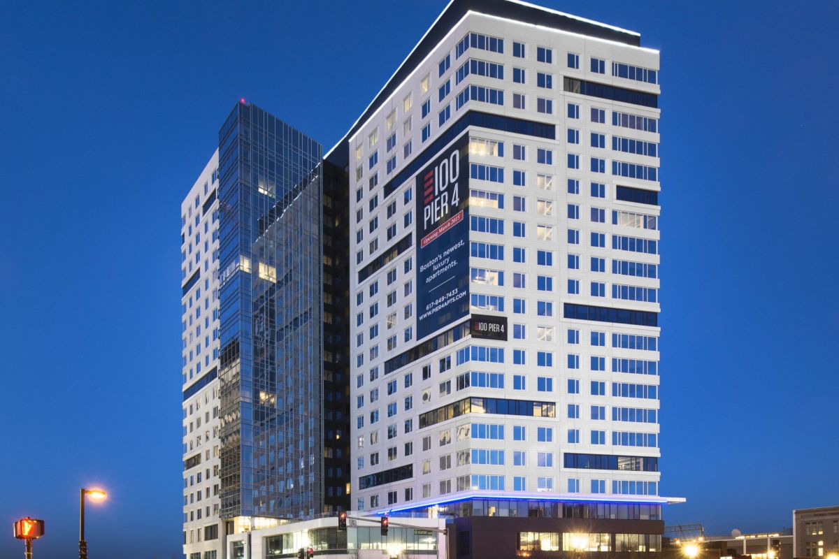 Modern high-rise building at dusk with illuminated windows and light trails from passing cars.