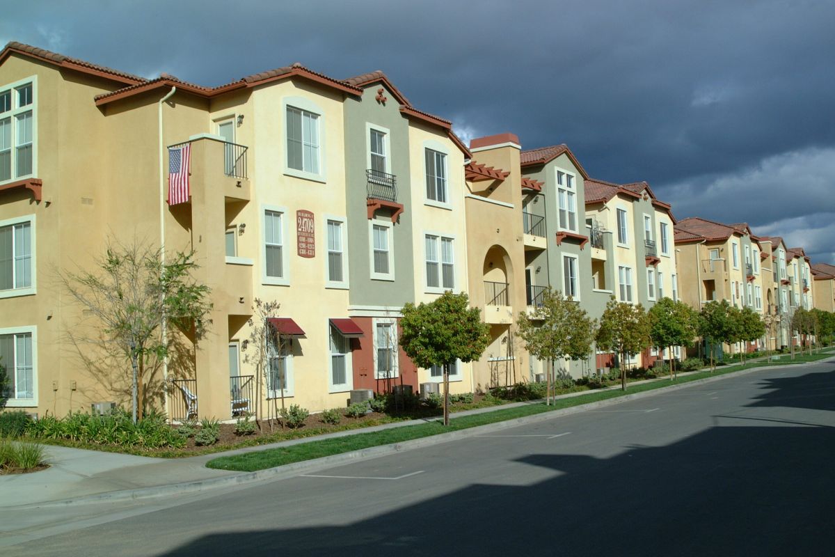 Row of colorful modern apartment buildings with balconies along a quiet, empty street under a cloudy sky.