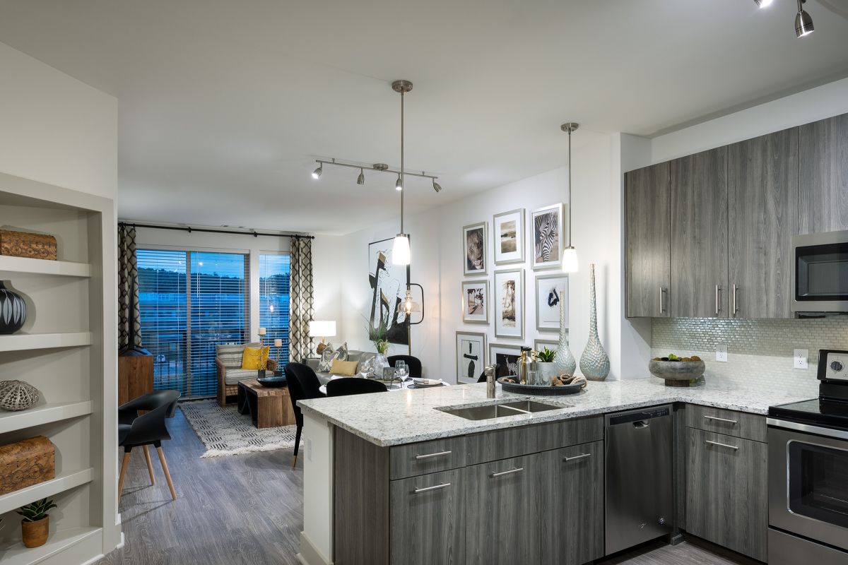 Modern apartment kitchen with gray cabinets, island, and open view to living and dining area with large windows.