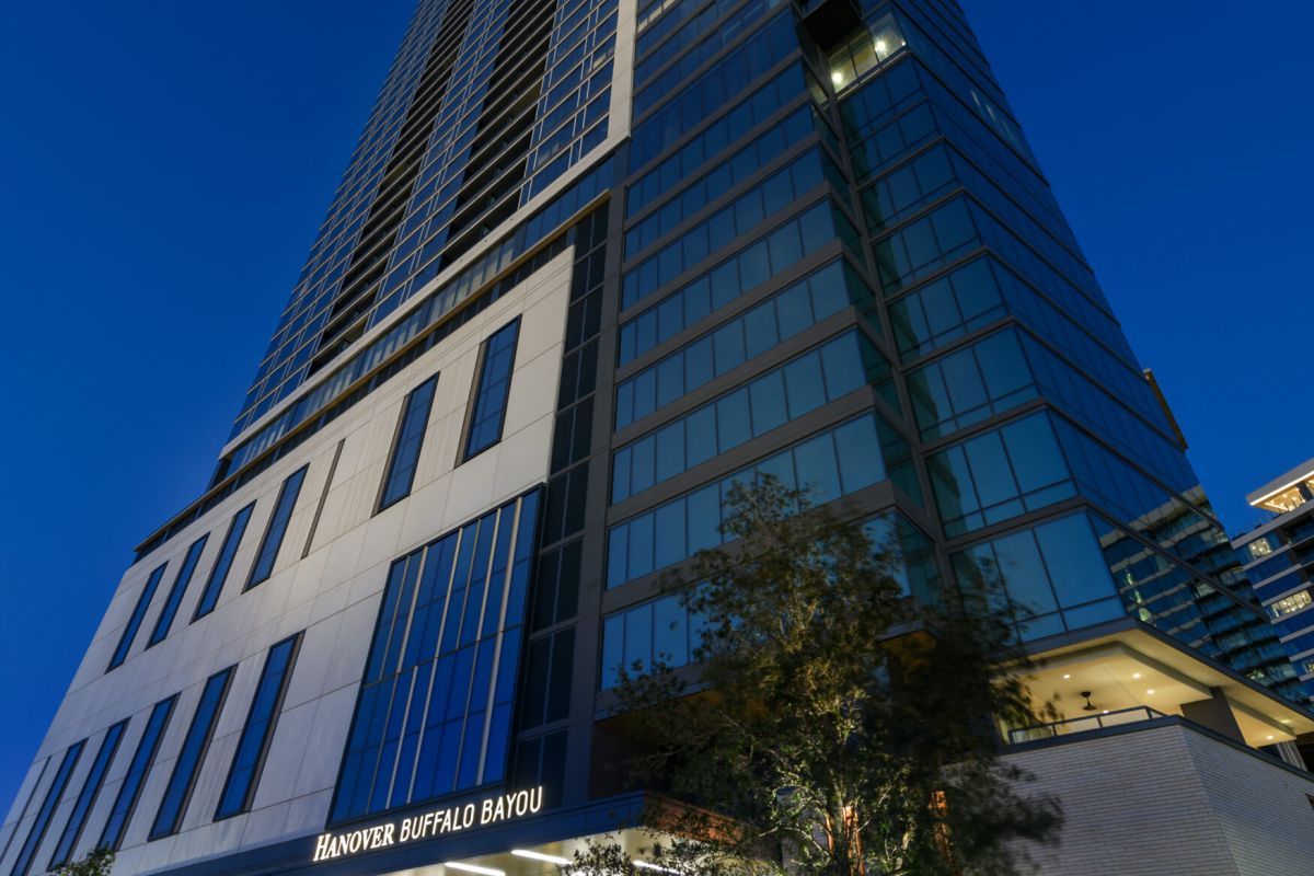 The Hanover Buffalo Bayou high-rise glows at night, with cars and trees lining the front in this vibrant cityscape.