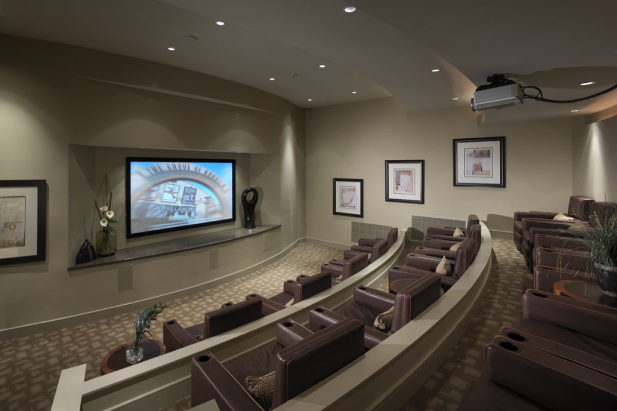 Small home theater room with rows of brown leather seats facing a large screen, modern decor.