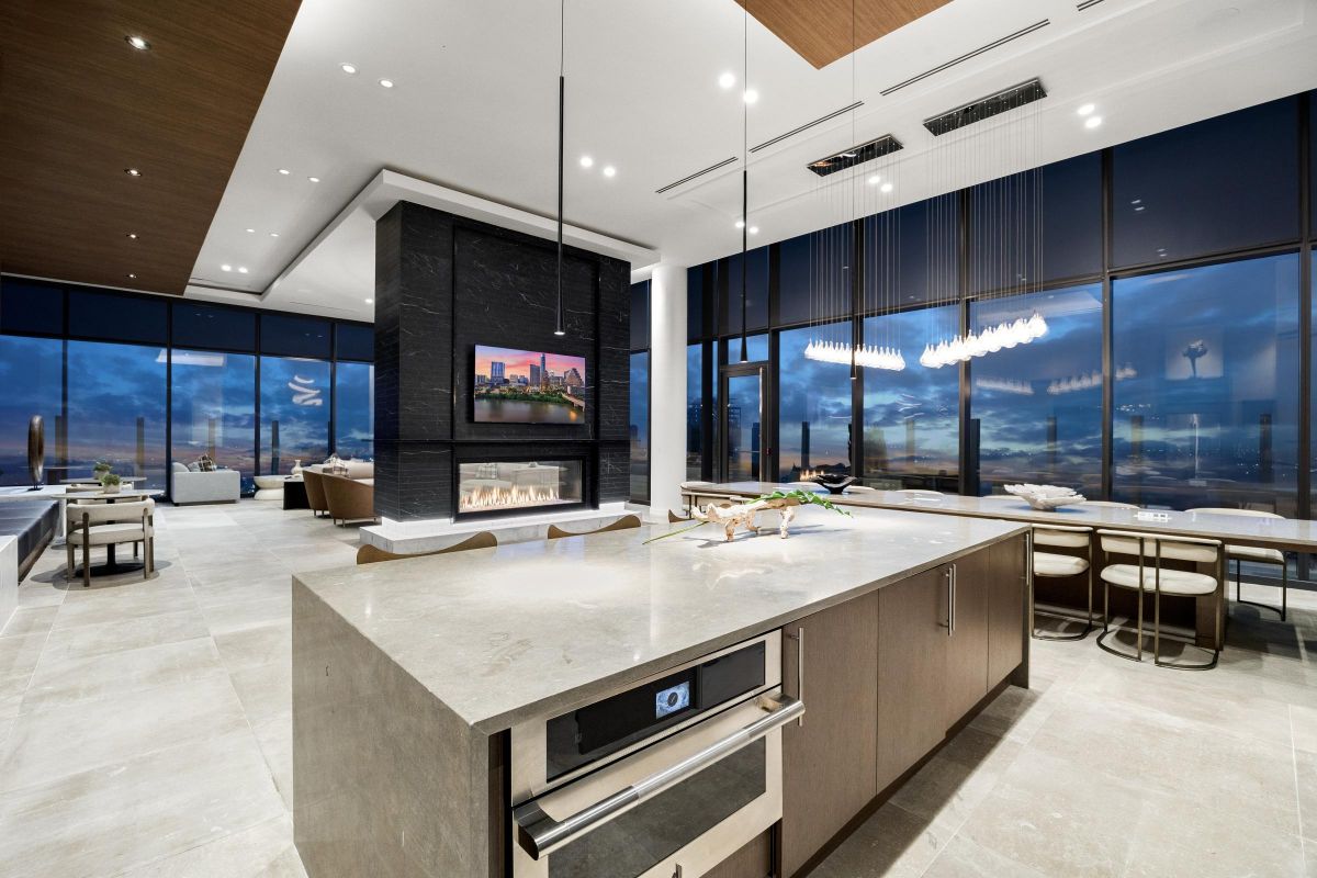 Modern kitchen and dining area with large windows, island counter, fireplace, and city skyline view at dusk.