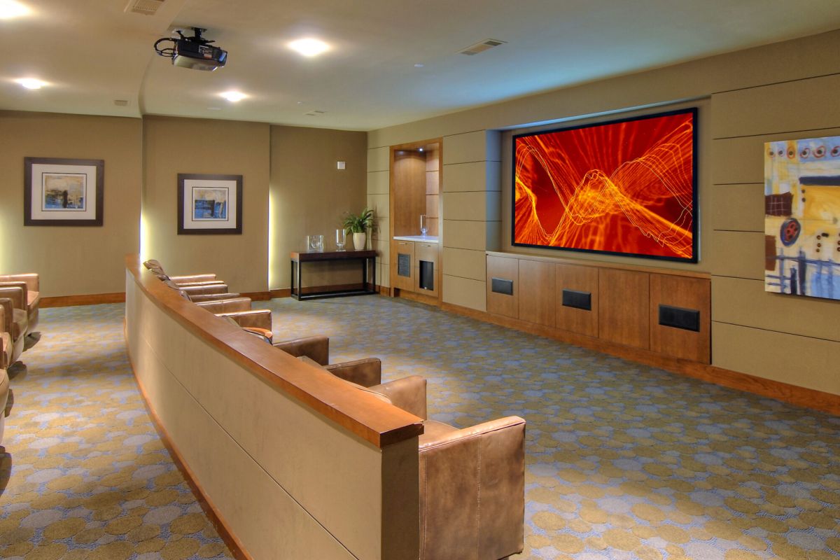 Modern home theater room with leather chairs, a large screen displaying abstract graphics, and wall art.