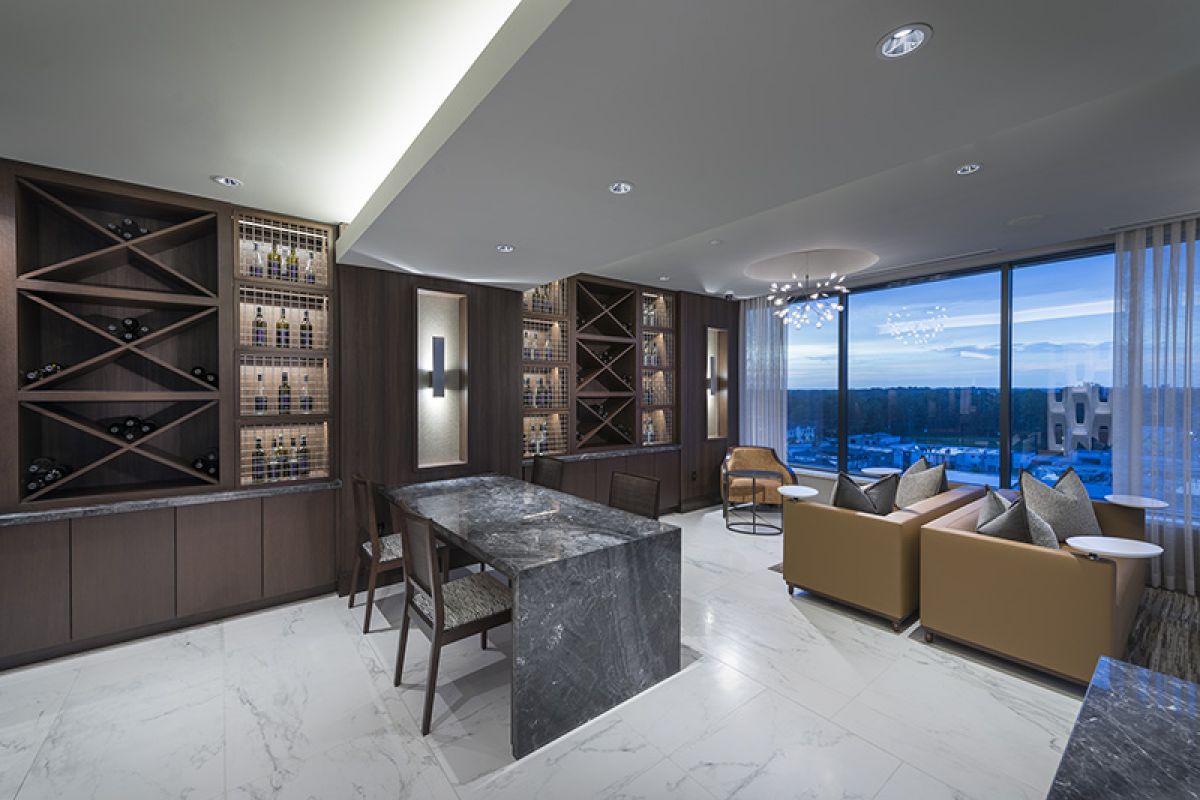 Modern lounge with marble floors, wine racks, a marble table, tan sofas, and large windows with a city view.