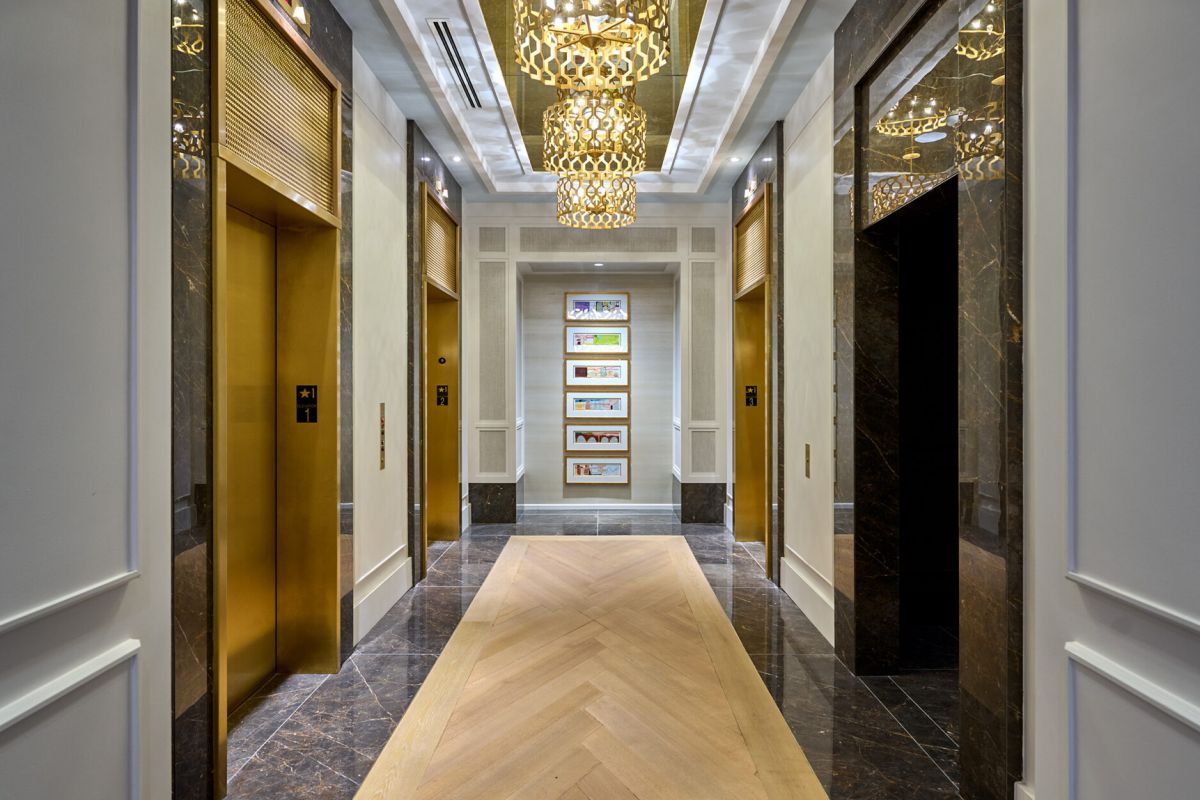 Elegant hallway with marble floors, Hanover gold elevators, and ornate chandeliers reflecting on the ceiling.