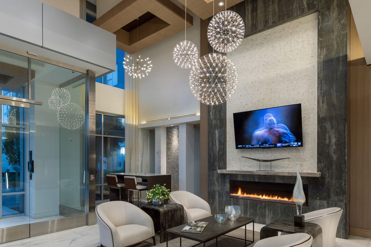 Modern lounge with white chairs, a fireplace, TV, marble floors, and spherical pendant lights hanging from the ceiling.