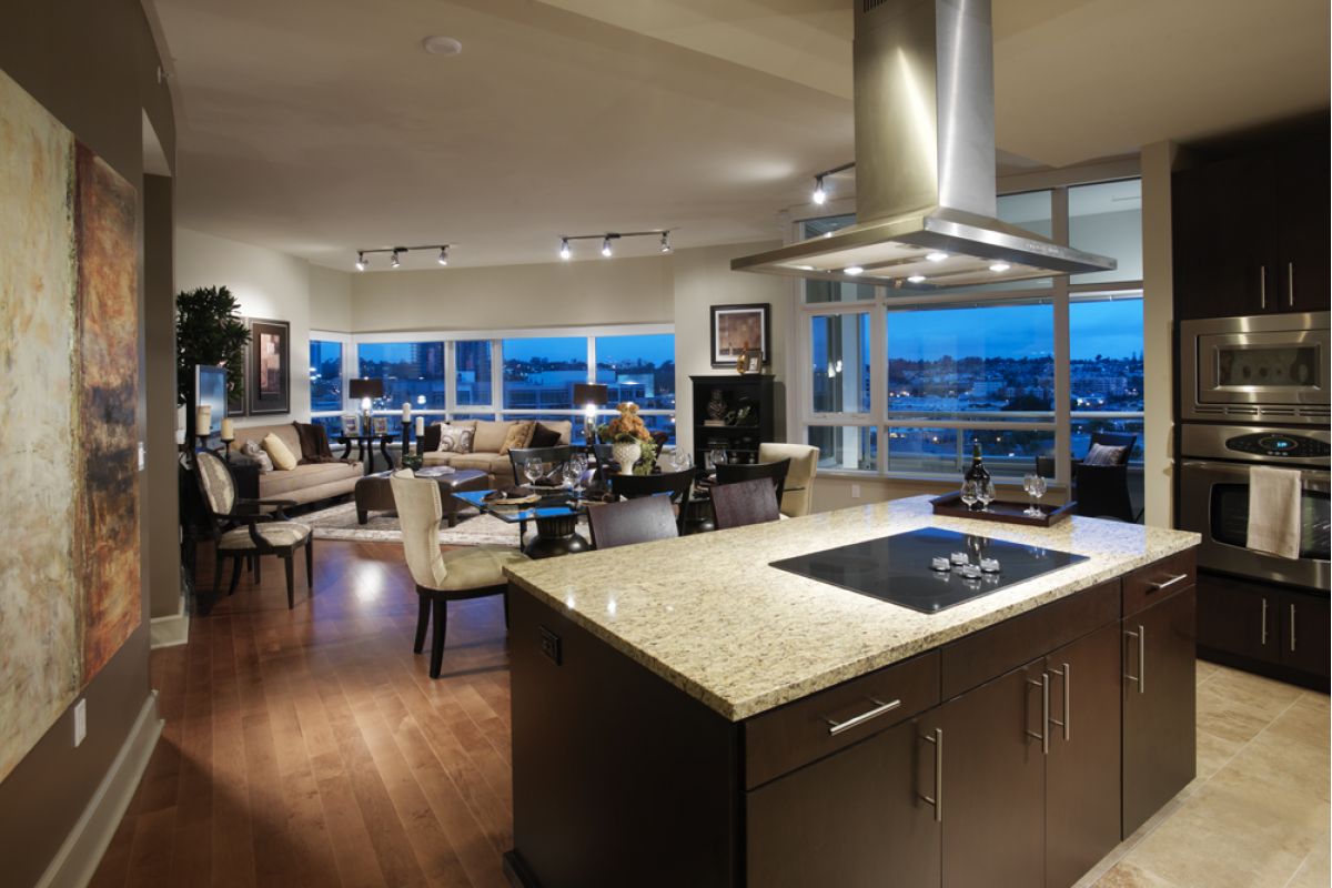 Modern open-concept kitchen and living room with large windows, city lights, and contemporary decor at dusk.