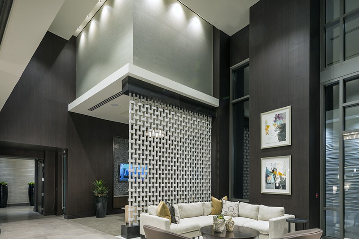 Modern lobby with high ceilings, neutral furniture, wall art, and geometric room divider under bright lighting.