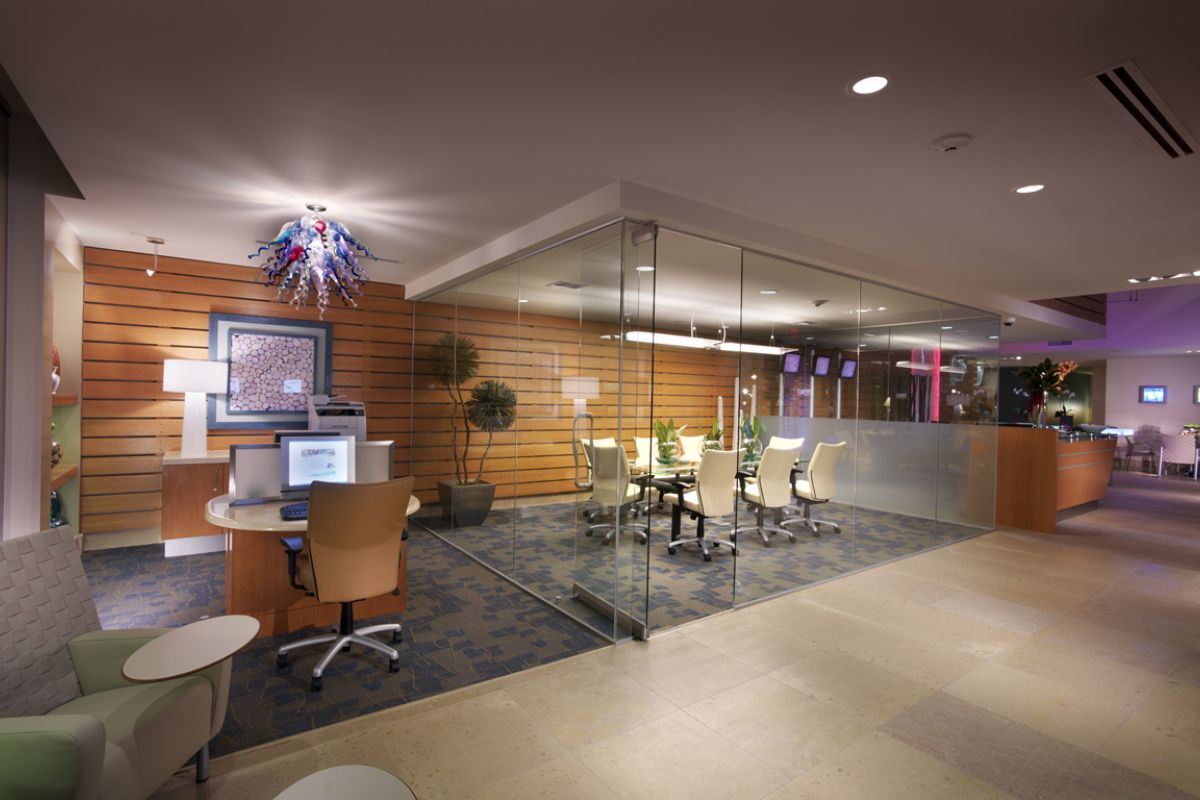 Modern office space with glass-walled meeting room, desks, chairs, and contemporary lighting.