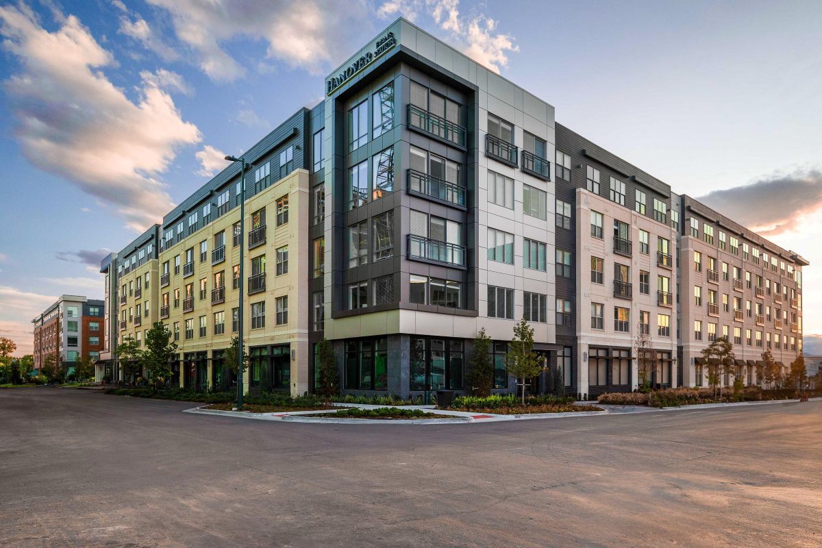 Modern multi-story building at sunset, featuring large windows and a mix of light beige and dark gray panels.
