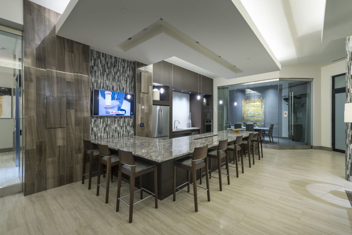Modern communal kitchen with bar seating, a TV on the wall, and dining area in the background at Hanover Shady Grove.
