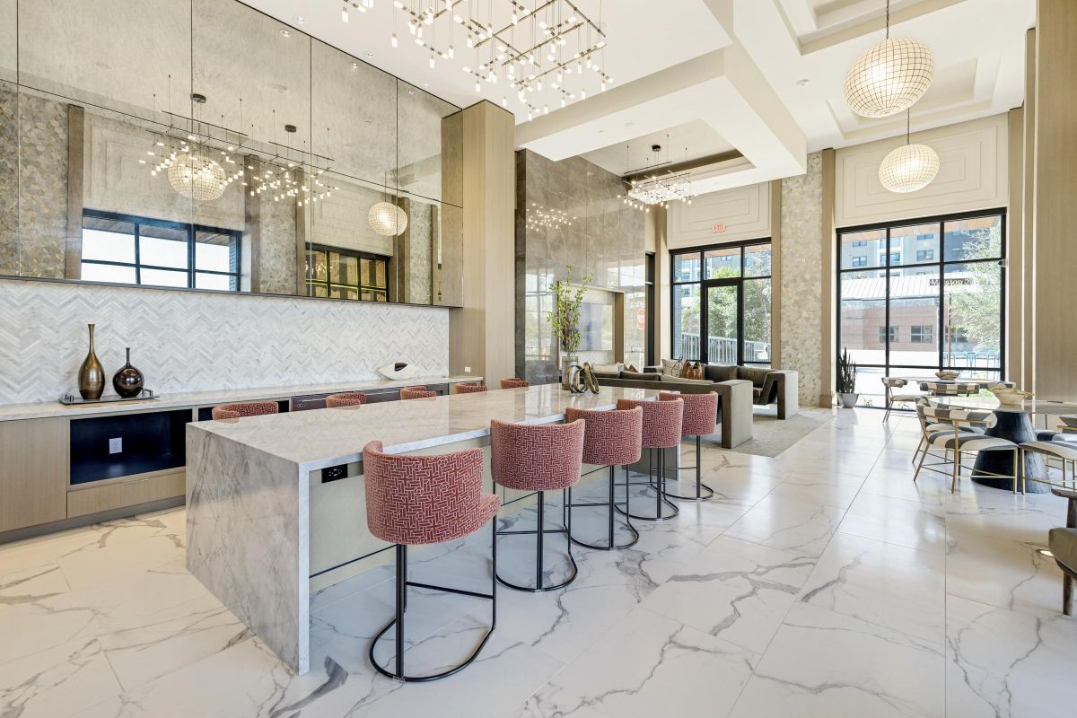 Modern kitchen with marble island, red barstools, and large windows. Geometric lights hang from the ceiling.