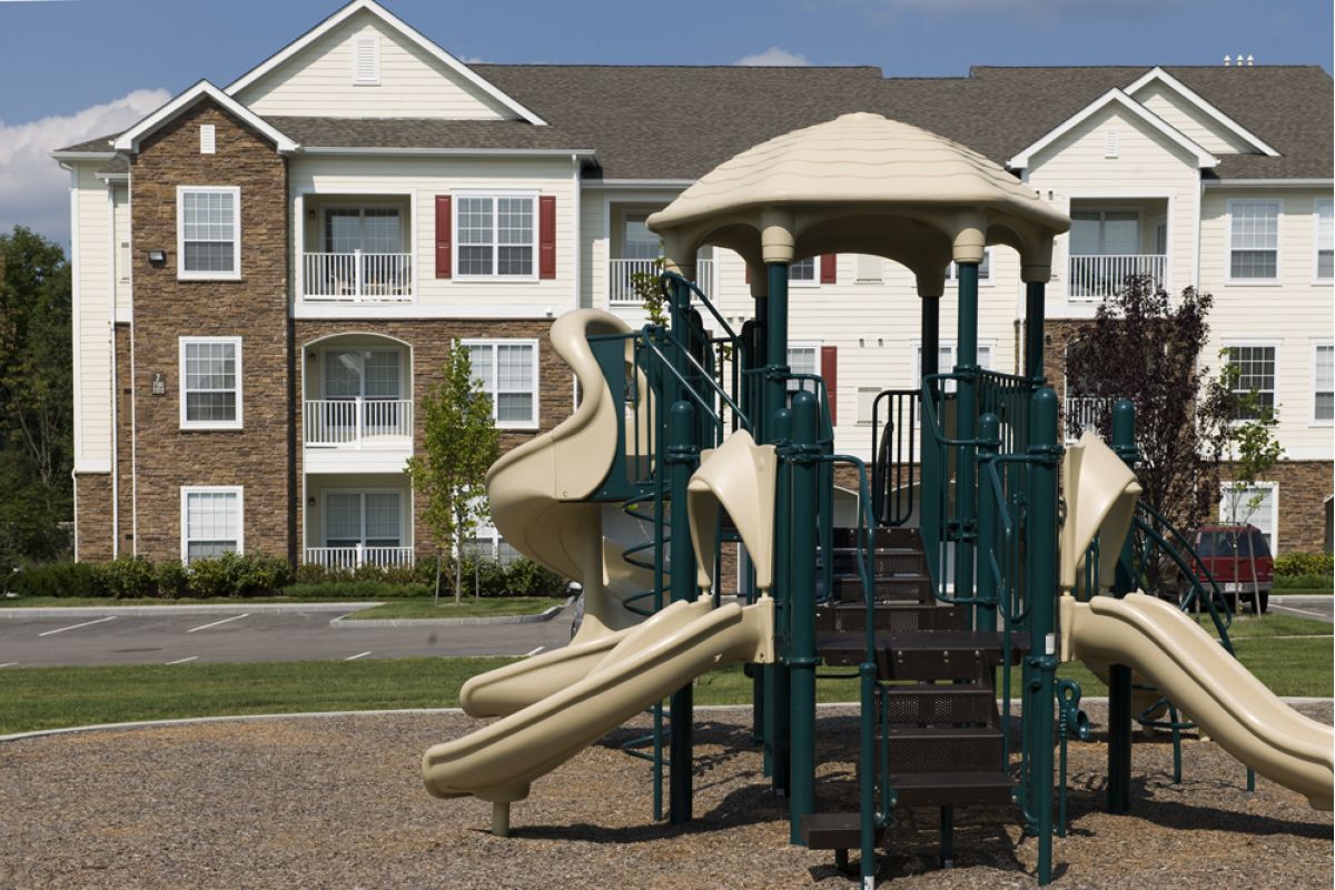 Playground with slides and climbing equipment in front of a multi-story apartment building.
