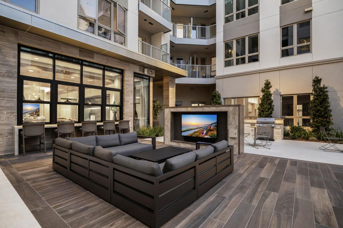 Hanover Laguna Niguel Modern apartment courtyard with a large sectional sofa, TV, outdoor kitchen, and patio seating.