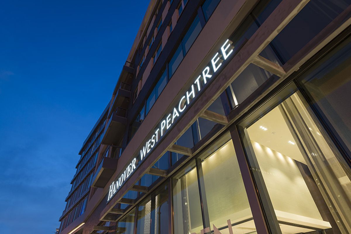 Modern building at dusk with illuminated "Hanover West Peachtree" sign above large glass windows.