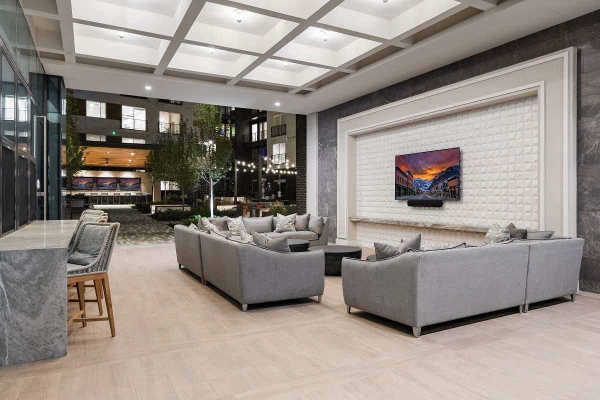 Modern lounge with gray sofas, large TV, and pool view through glass doors; elegant ceiling lights above.