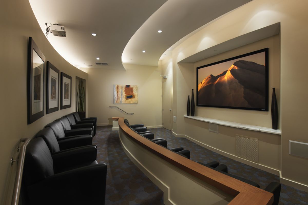 A small, modern home theater with black chairs facing a large screen displaying a mountain landscape.