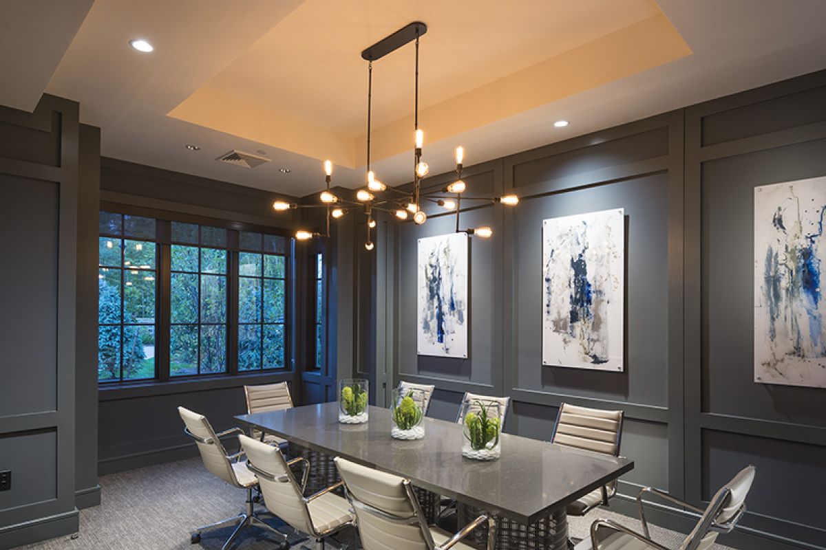 Modern conference room with a long table, six chairs, abstract art, and large windows showing greenery.