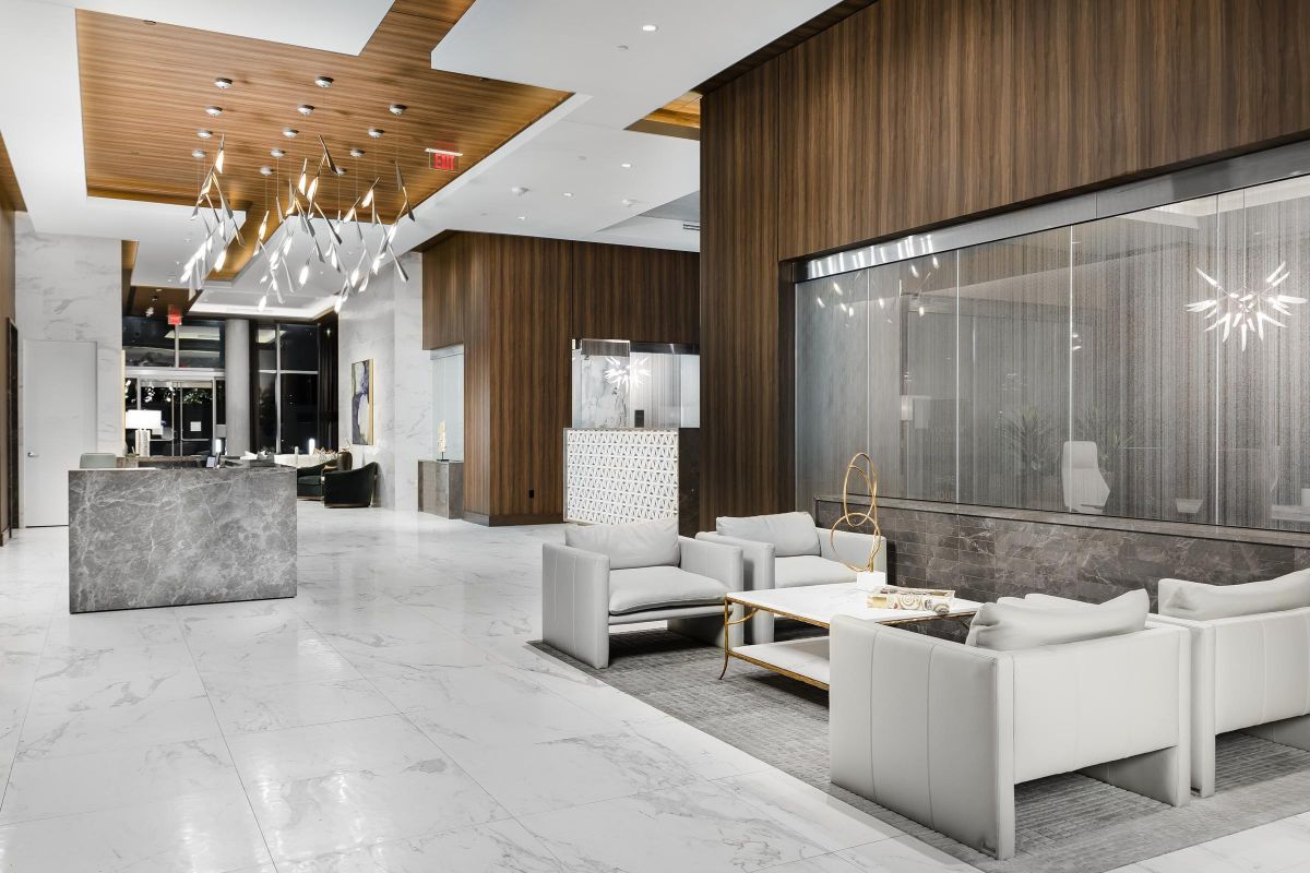 Modern hotel lobby with marble floors, white sofas, wooden accents, and contemporary lighting fixtures.