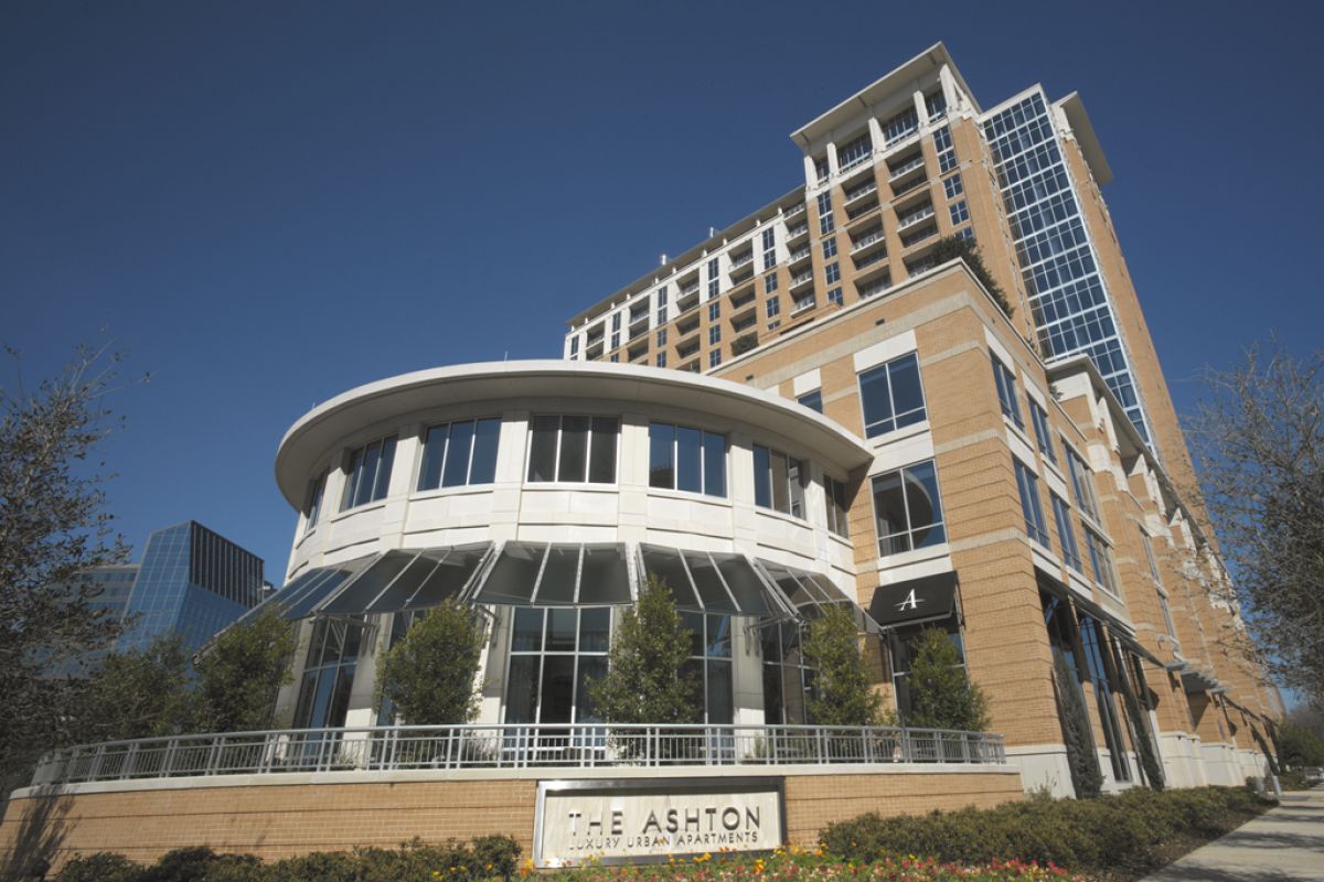 Modern multi-story apartment building with large windows and a sign reading "The Ashton" in front.