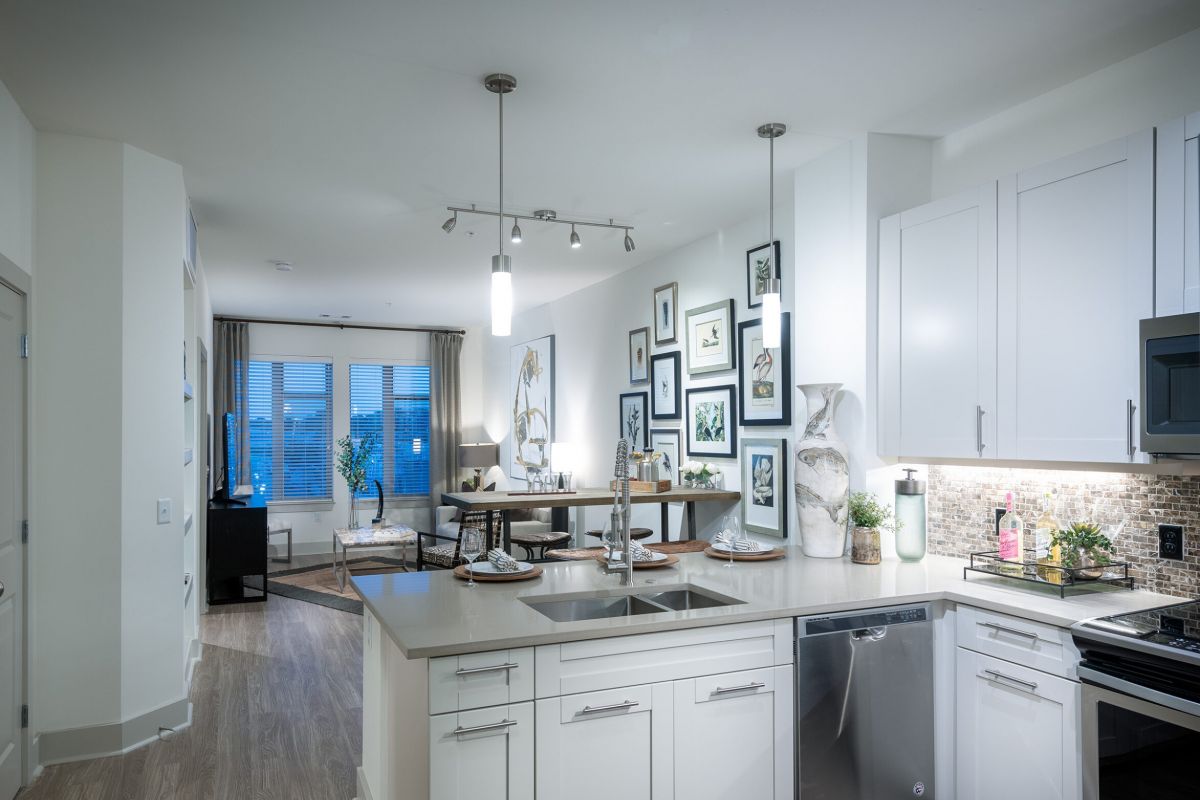 Modern kitchen with white cabinets, stainless steel appliances, and open layout to a living and dining area.
