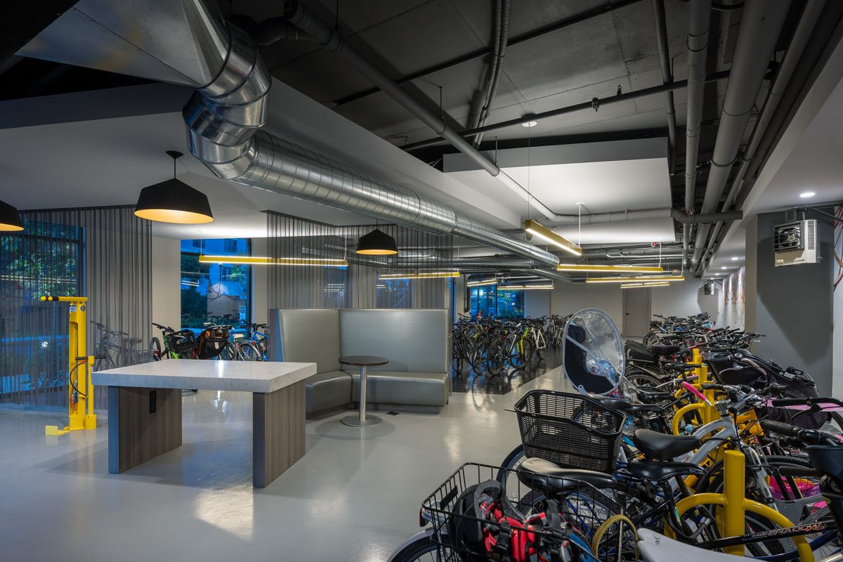 Modern indoor bike storage room with numerous bicycles, yellow repair stands, and industrial lighting.
