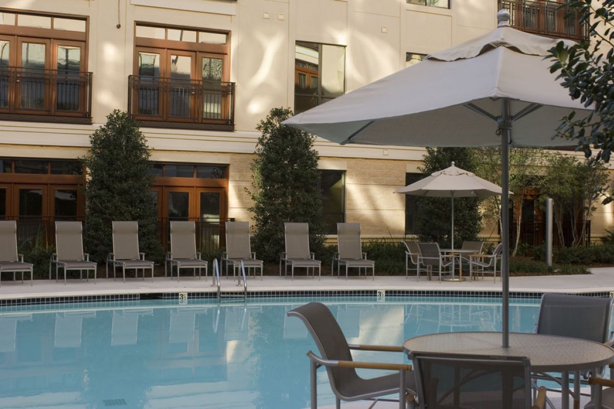 Outdoor pool with lounge chairs, tables, and umbrellas in front of a modern building.