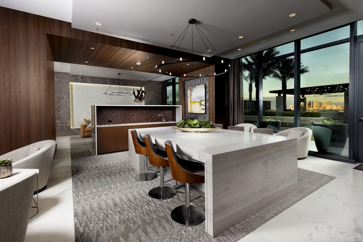 Modern kitchen with a marble island, bar stools, a chandelier, and floor-to-ceiling windows showing a cityscape.