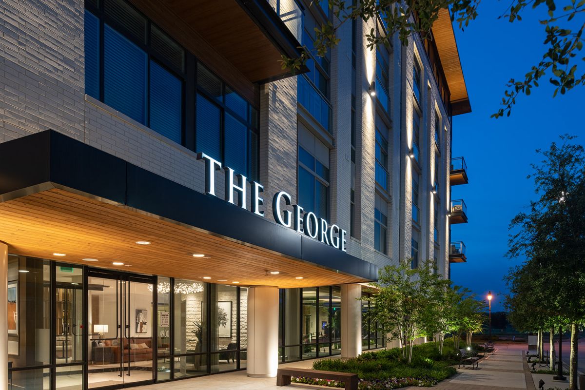Modern hotel entrance at dusk with "The George" sign, large windows, benches, and landscaped walkway.